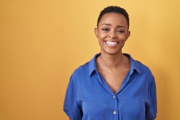 African american woman standing over yellow background with a happy and cool smile on face. lucky...