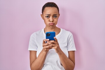 Beautiful african american woman using smartphone puffing cheeks with funny face. mouth inflated with air, catching air.