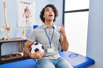 Hispanic man with curly hair working as football physiotherapist amazed and surprised looking up...