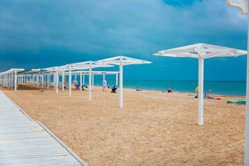 White wooden poles on the sandy beach for umbrellas and awnings. Bathing and resting people on a sunny day.