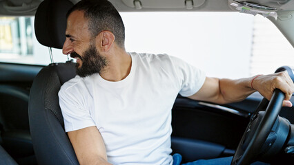 Young hispanic man driving car looking back at street