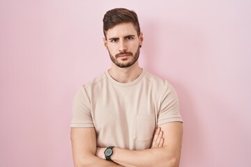 Hispanic man with beard standing over pink background skeptic and nervous, disapproving expression on face with crossed arms. negative person.