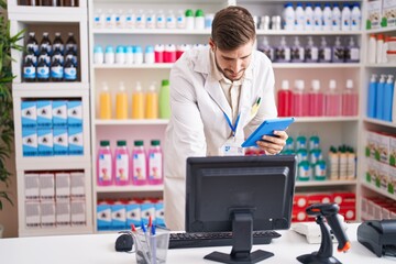 Young caucasian man pharmacist using computer and touchpad at pharmacy