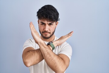 Naklejka premium Hispanic man with beard standing over white background rejection expression crossing arms doing negative sign, angry face