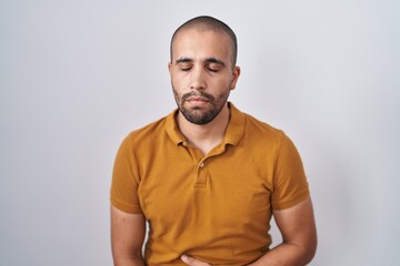 Hispanic man with beard standing over white background with hand on stomach because indigestion, painful illness feeling unwell. ache concept.