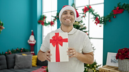 Obraz na płótnie Canvas Young hispanic man smiling confident holding christmas gift at home