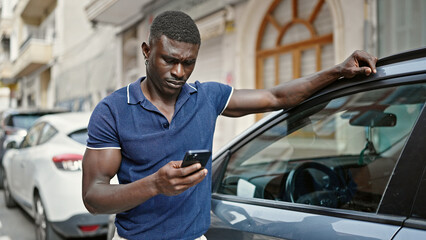 Fototapeta na wymiar African american man using smartphone leaning on car at street