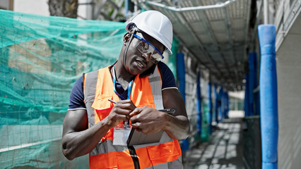 African american man builder using touchpad talking on smartphone at construction place