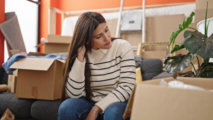 Young beautiful hispanic woman sitting on sofa with serious expression at new home