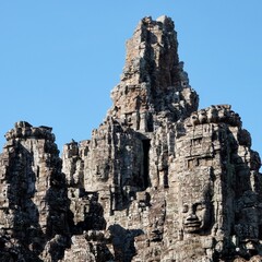 Fototapeta na wymiar The majestic stone towers of the Bayon Temple in Cambodia, an iconic symbol of Khmer architecture, under a clear blue sky.