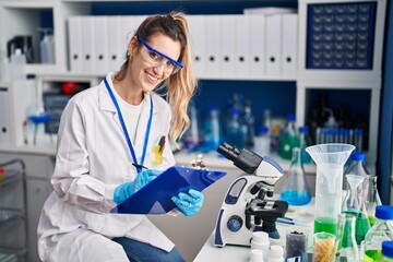 Young woman scientist smiling confident writing medical report at laboratory