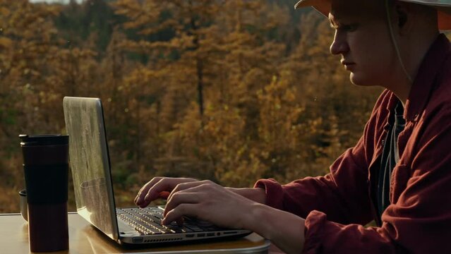 Travel notes, middle-aged man professionally Works remotely sitting in the mountains looking into a laptop outdoors. The concept of a stylish man Cognition of the inner world of wildlife
