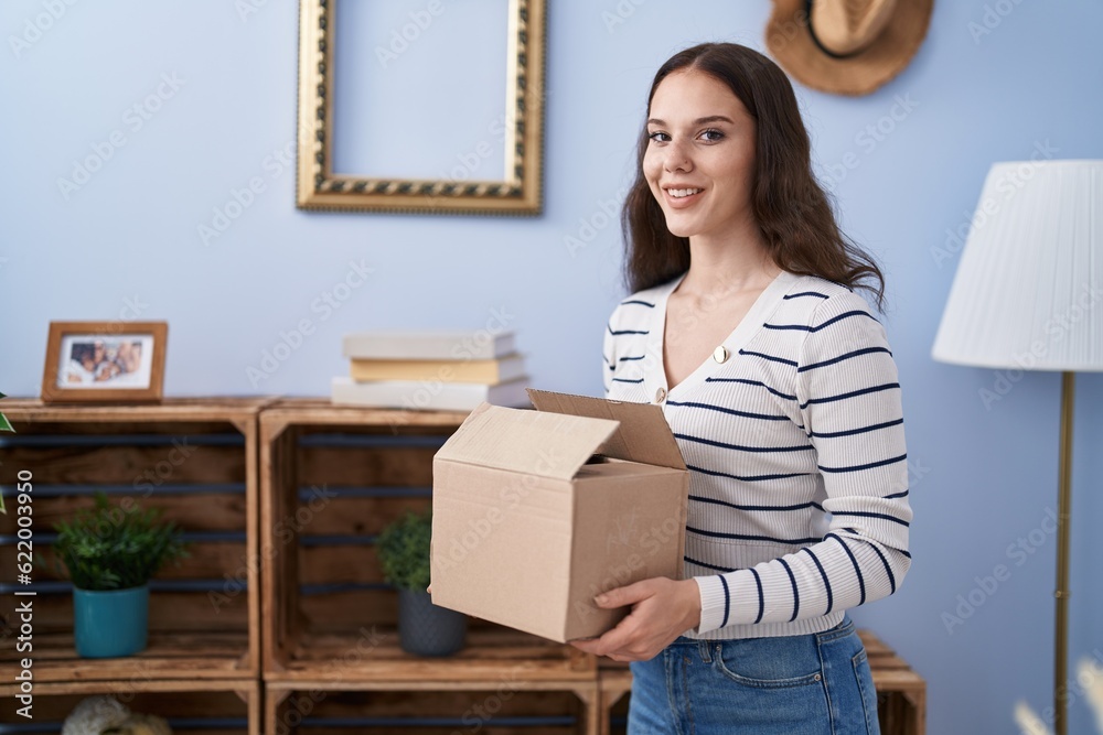 Sticker Young woman smiling confident holding package at home