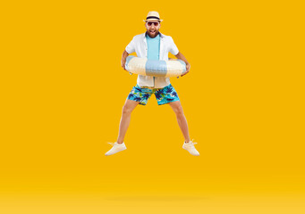 Happy funny man in summer clothes and sunglasses holding inflatable beach ring and jumping on...