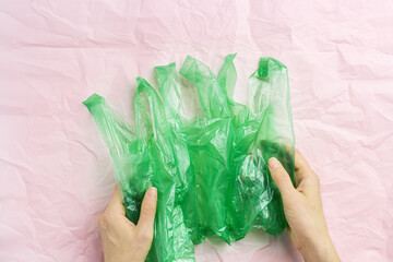 Green plastic bags in woman hands on pink crumpled paper background, conscious lifestyle concept, minimal style image. Single-use plastic ban. Eco trend to reduce disposable plastics, top