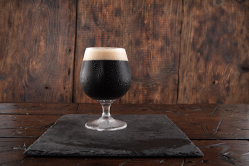 A glass of dark beer on a wood background. Beer on a slate tray. Serving stout beer.