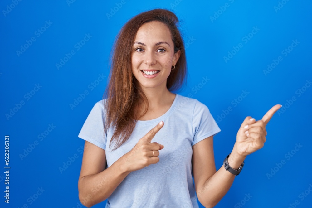 Sticker brunette woman standing over blue background smiling and looking at the camera pointing with two han