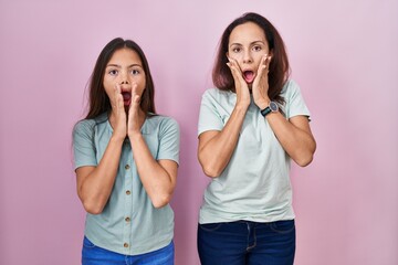Young mother and daughter standing over pink background afraid and shocked, surprise and amazed...