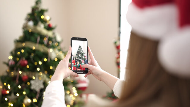 Young blonde woman make photo to christmas tree by smartphone at home