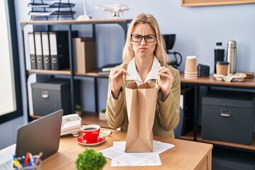 Young caucasian woman working at the office holding paper bag skeptic and nervous, frowning upset because of problem. negative person.