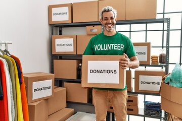 Middle age grey-haired man volunteer smiling confident holding donations package at charity center