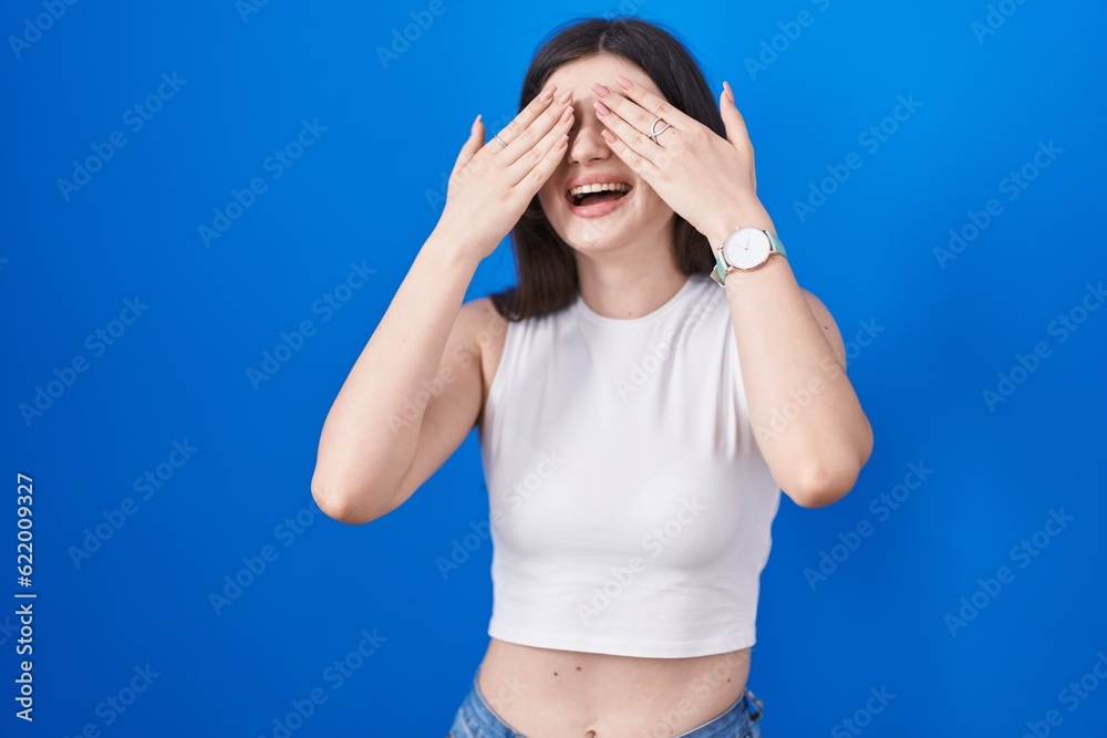 Canvas Prints Young caucasian woman standing over blue background covering eyes with hands smiling cheerful and funny. blind concept.