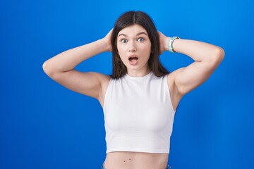 Fototapeta na wymiar Young caucasian woman standing over blue background crazy and scared with hands on head, afraid and surprised of shock with open mouth