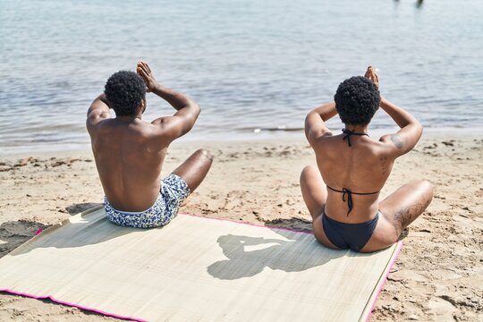 African american man and woman couple wearing swimsuit doing yoga exercise at seaside