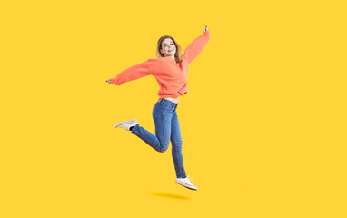 Fototapeta na wymiar Overjoyed millennial girl isolated on yellow studio background jump dance. Smiling young Caucasian woman have fun make dancer moves enjoy loud music. Entertainment and hobby.
