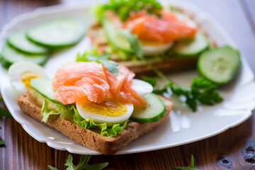 fried toast with lettuce, egg, cucumbers and red fish in a plate.