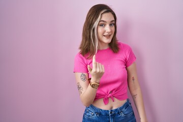 Blonde caucasian woman standing over pink background beckoning come here gesture with hand inviting welcoming happy and smiling