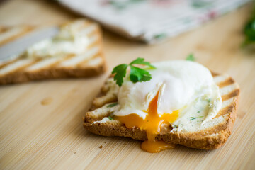 Fried toast bread with spread and poached egg, on a wooden table.