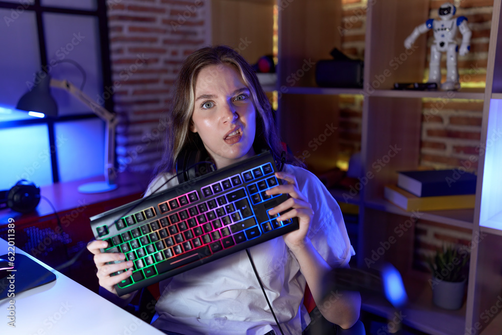 Poster young caucasian woman holding gamer keyboard clueless and confused expression. doubt concept.