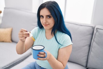 Young caucasian woman pouring liquid on cup sitting on sofa at home