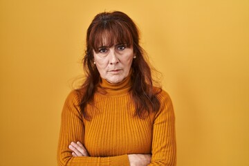Middle age hispanic woman standing over yellow background skeptic and nervous, disapproving expression on face with crossed arms. negative person.