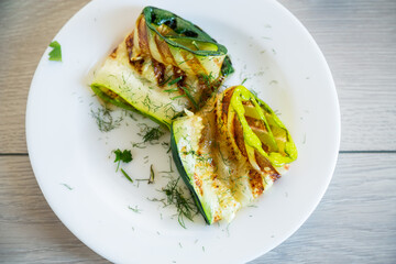 Grilled zucchini pieces with garlic sauce in a white plate.