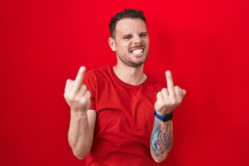 Young hispanic man standing over red background showing middle finger doing fuck you bad...