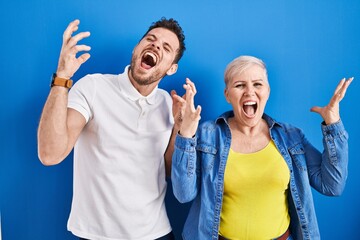 Young brazilian mother and son standing over blue background celebrating mad and crazy for success with arms raised and closed eyes screaming excited. winner concept