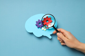 Paper brain on blue background and hand with  lens