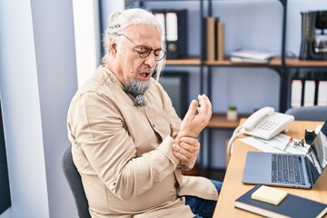 Middle age grey-haired man business worker suffering for wrist pain working at office