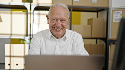 Senior grey-haired man ecommerce business worker using laptop sitting with arms crossed gesture at office