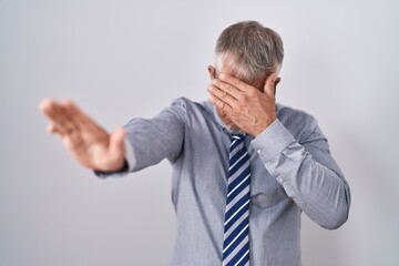 Hispanic business man with grey hair wearing glasses covering eyes with hands and doing stop gesture with sad and fear expression. embarrassed and negative concept.