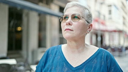 Middle age grey-haired woman looking to the sky with serious expression at street