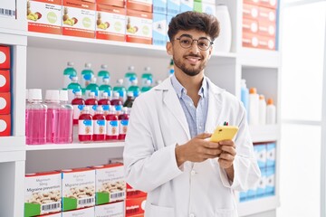 Young arab man pharmacist using smartphone standing at pharmacy