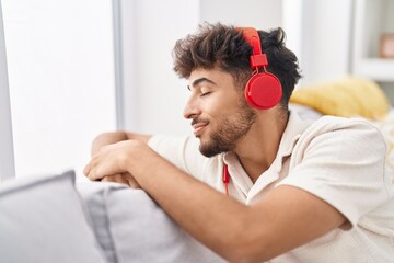 Young arab man listening to music sitting on sofa at home