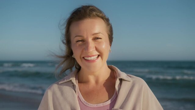 Happy girl with beautiful green eyes openly smiling laughing, looking at camera. Natural beauty face female 30s. Gorgeous woman slow motion 4K. Close up of young womans face, wind blowing blonde hair