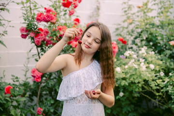 Beautiful teenage girl in a white dress picking cherries or cherries, looks at her