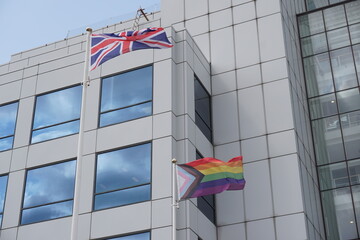 Union Jack flag and Pride flag outside city building flying in the wind. 