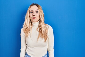 Young caucasian woman standing over blue background smiling looking to the side and staring away thinking.