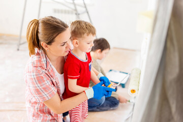 Mother with her children painting the wall with paint using roller and brush